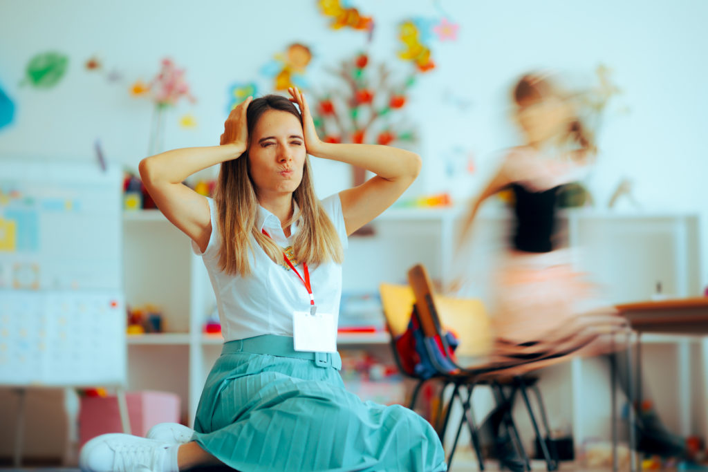Stressed teacher in chaotic classroom.